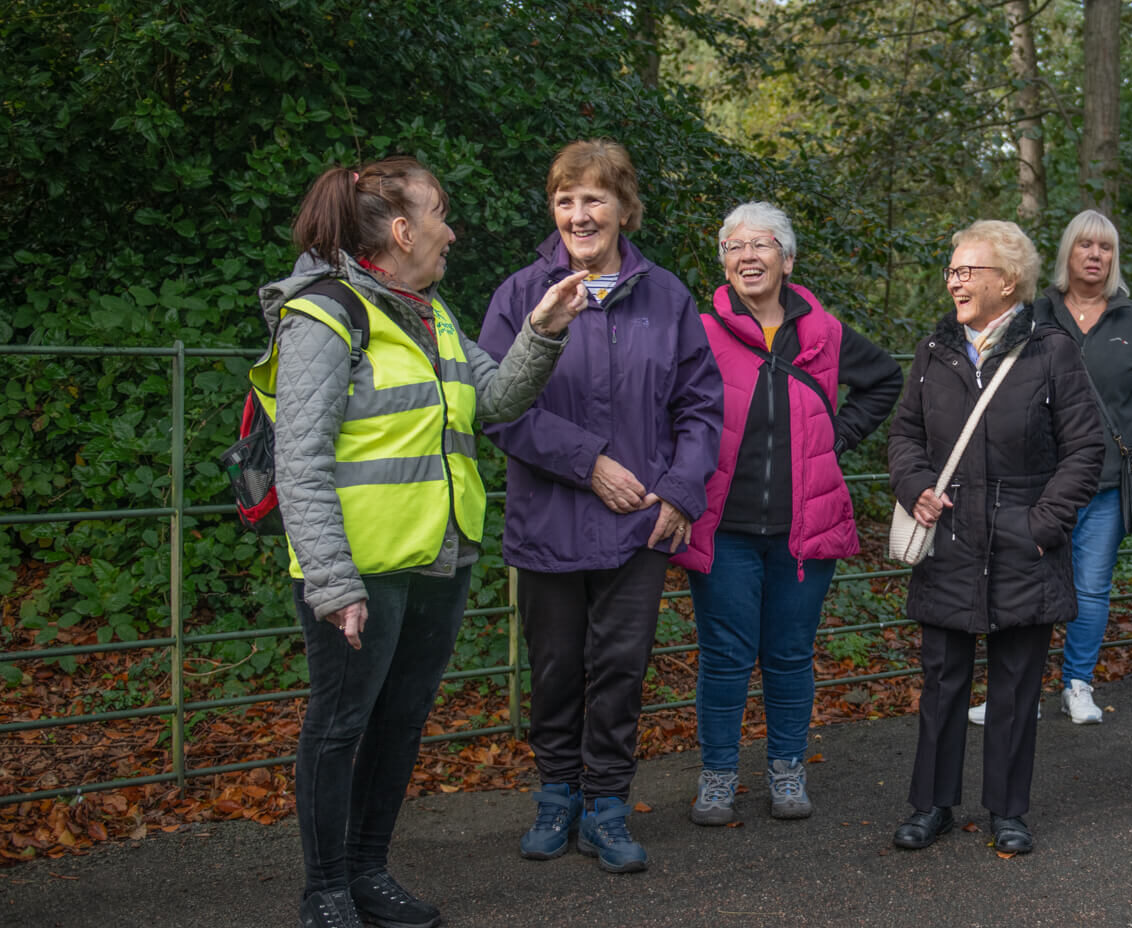 A group of people in a park looking at a health walk leader telling a story