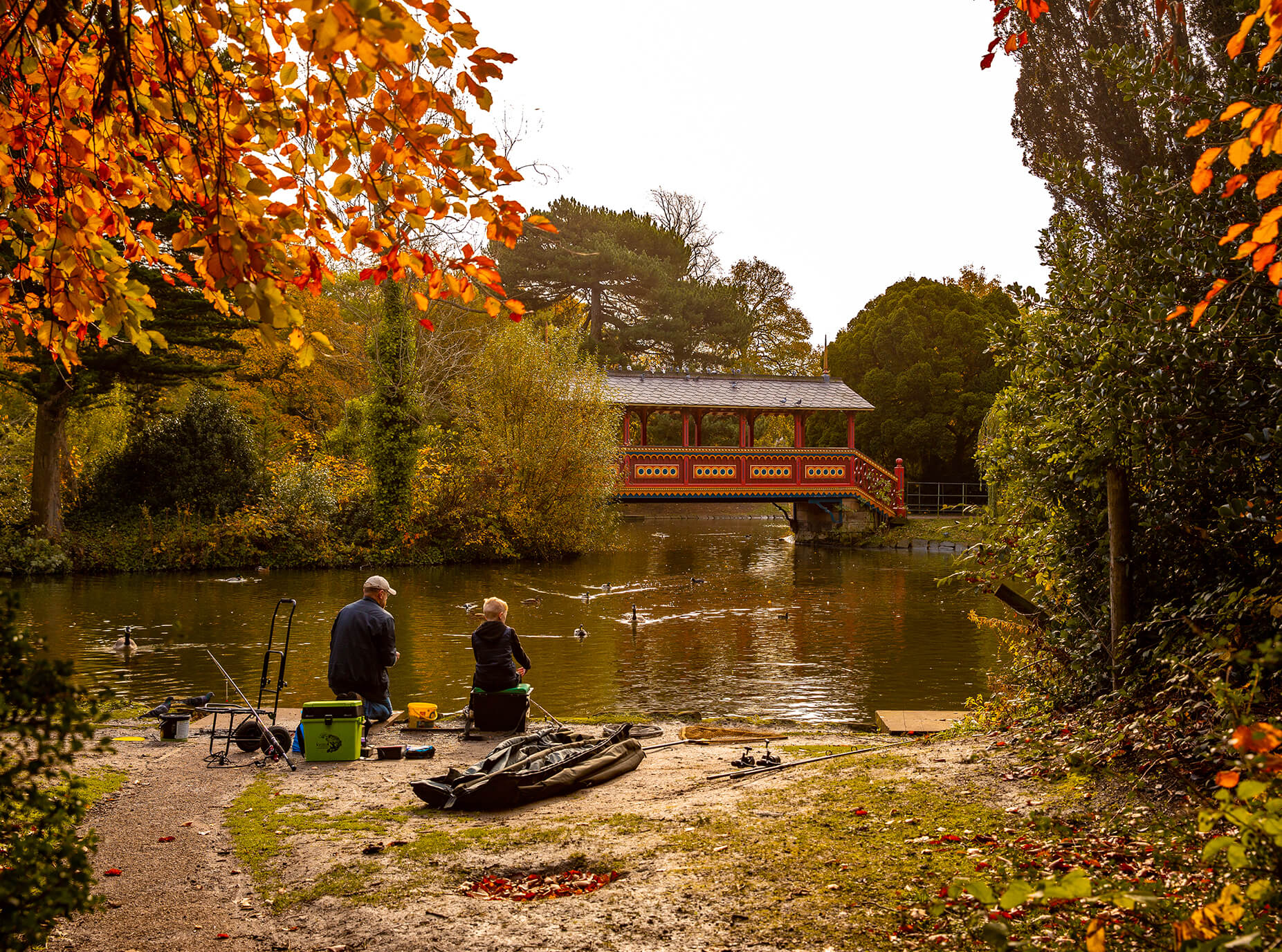 A man and child fishing at Birkenhead Park next to the red Swiss Bridge