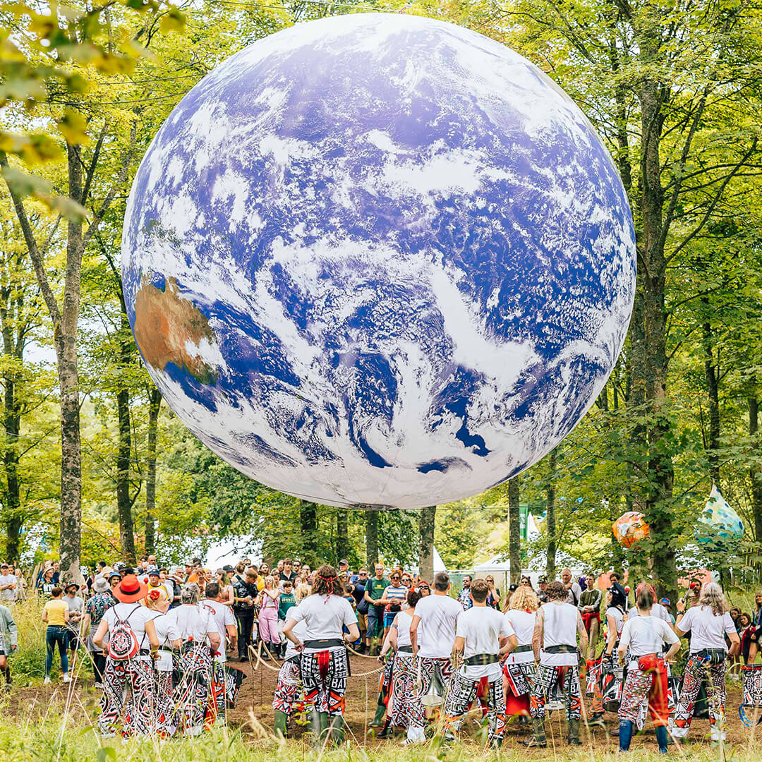 An enlarged Earth replica floating artwork displayed in a forest with a crowded gathering